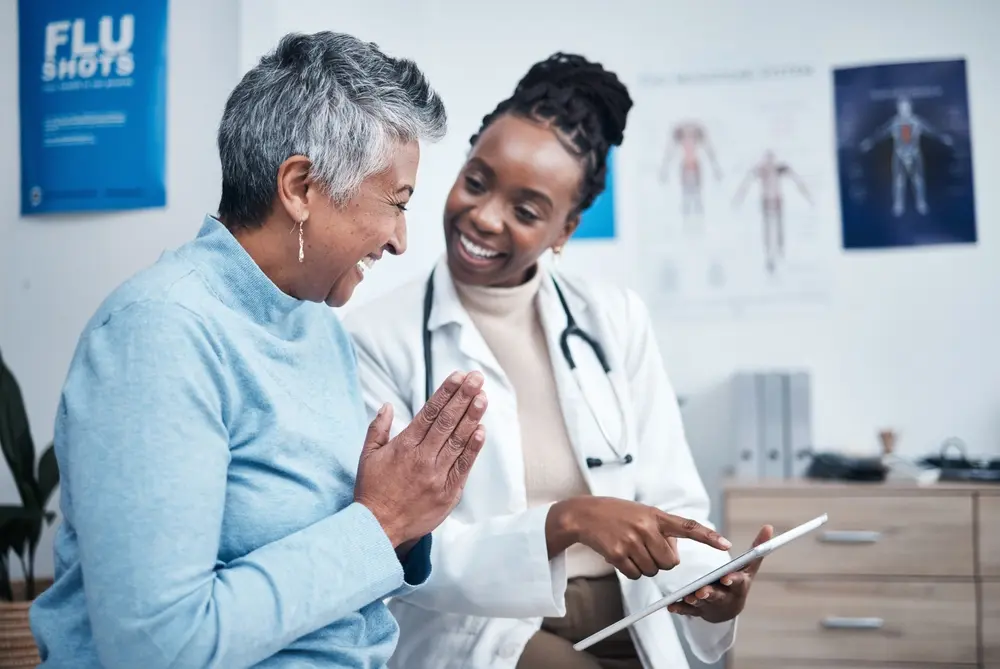 Black woman doctor and elderly patient sharing good news using a tablet.